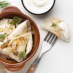 zdjęcie pierogów bezglutenowych w glinianym naczyniu, ze smażoną cebulką z widelcem obok