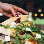 zdjęcie kawałka pinsy bezglutenowej z dodatkami trzymanego przez kobiecą dłoń