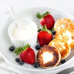 zdjęcie bezglutenowych placków ułożonych na białym talerzu, w towarzystwie truskawek, jagód i białego sosu