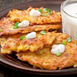 zdjęcie bezglutenowych placków ziemniaczanych podanych na talerzu w towarzystwie śmietany, szczypiorku i dodatkowego sosu w szklance obok