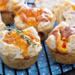 Mini quiche bez glutenu z ciastem francuskim, rumiane i złociste, z kremowym nadzieniem jajecznym i dodatkami, studzące się na kratce kuchennej.