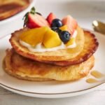 zdjęcie racuchów bezglutenowych ułożonych w stosik na talerzu i udekorowanych owocami