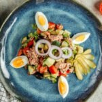 zdjęcie bezglutenowej sałatki z tuńczykiem, jajkiem i warzywami na niebieskim glinianym talerzu ustawionym na stole kuchennym