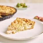 zdjęcie kawałka bezglutenowej szarlotki z kruszonką odkrojonego z foremki, ułożonego na białym talerzu ze złotą obwódką