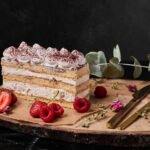 Bezglutenowy biszkoptowy deser warstwowy z kremem, podany jako kawałek ciasta na drewnianej desce z owocami