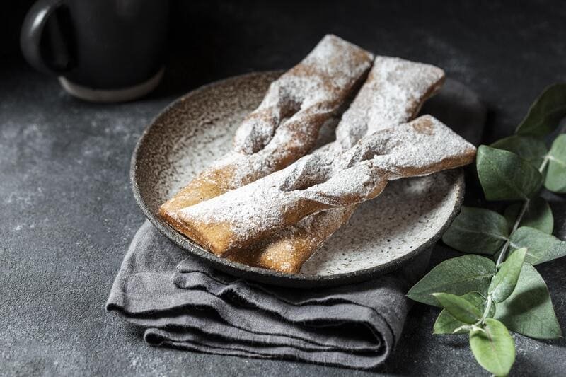 Bezglutenowe faworki posypane cukrem pudrem, podane na ceramicznym talerzu w domowym otoczeniu
