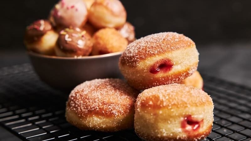 Bezglutenowe pączki z cukrem i nadzieniem malinowym, część z polewą czekoladową, na kratce kuchennej