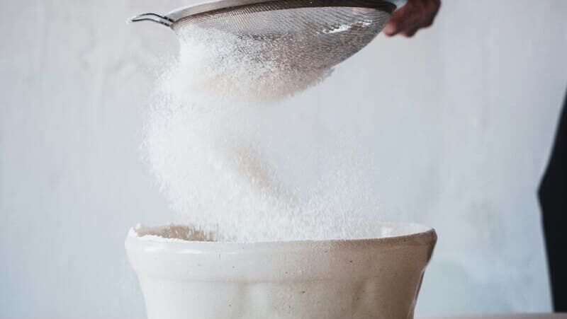 Przesiewanie mąki ryżowej do miski podczas przygotowania bezglutenowych wypieków