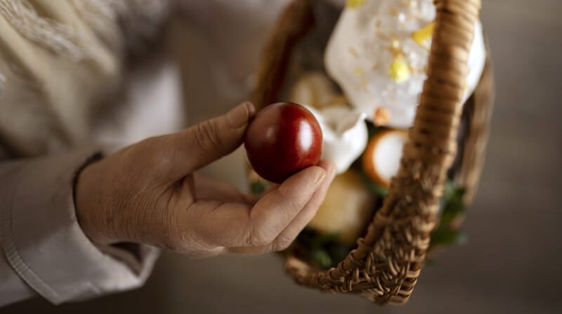 Święconka wielkanocna w koszyku – ręka trzyma czerwone jajko, w tle tradycyjne produkty wielkanocne