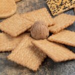 Prostokątne herbatniki ułożone promieniście na ciemnym blacie, jeden orzech włoski pośrodku, naturalna stylizacja i miękkie światło.