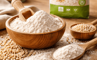 Mąka z sorgo bezglutenowa rozsypana na drewnianym stole w kuchni, w tle rozmyte opakowanie bio mąki i składniki