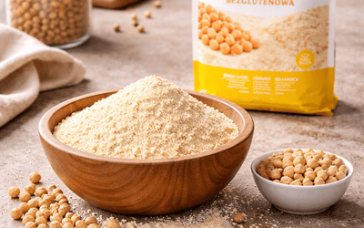 Mąka z ciecierzycy bezglutenowa w misce na stole, wokół rozsypane ziarna ciecierzycy, w tle rozmyte opakowanie produktu