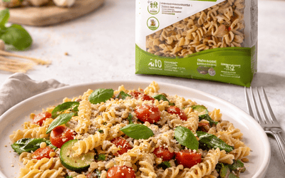 Makaron owsiany bezglutenowy fusilli z warzywami na talerzu w jasnej kuchni, w tle rozmyte opakowanie bio makaronu i świeże składniki