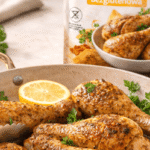 Pieczone pałki z kurczaka z przyprawą bezglutenową w naczyniu na stole, w tle rozmyte opakowanie przyprawy i świeże zioła