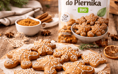 Bezglutenowe pierniczki dekorowane lukrem na drewnianej desce, w tle rozmyte opakowanie przyprawy do piernika i świąteczne dodatki