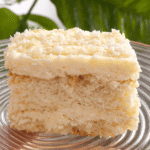 Kawałek bezglutenowego ciasta rafaello na szklanym talerzu – kokosowy deser z kremową warstwą i wiórkami kokosowymi, podany w naturalnym świetle.