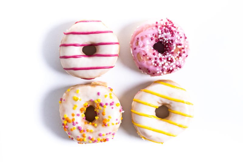 Słodkie pączki bez glutenu z kolorową polewą i posypką na białym tle.