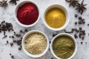 Naturalne przyprawy bez glutenu w małych miseczkach – kolorowe proszki i całe przyprawy na jasnym tle.