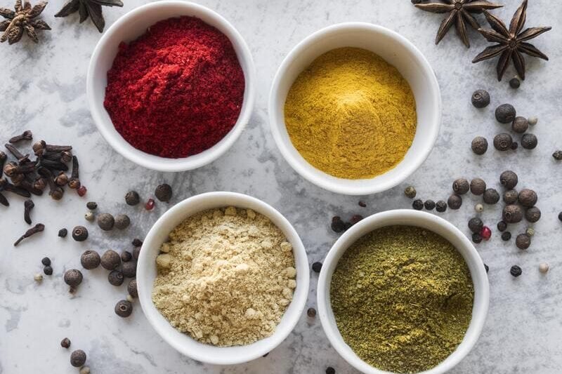 Naturalne przyprawy bez glutenu w małych miseczkach – kolorowe proszki i całe przyprawy na jasnym tle.