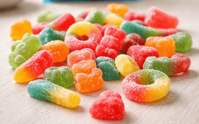 Kolorowe żelki bezglutenowe rozsypane na stole w domowej kuchni, w tle rozmyte opakowanie cukierków owocowych