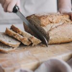 Chleb z serka wiejskiego bez mąki, jasny i jednolity w strukturze, miękki w środku i lekko zarumieniony na zewnątrz, pokrojony na kromki, podany na drewnianej desce w domowym otoczeniu