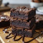 Fit brownie bez mąki, wilgotne i czekoladowe, pokrojone na kawałki i ułożone na drewnianej desce, polane czekoladą i posypane solą, w domowym otoczeniu