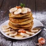 Fit placuszki z serka wiejskiego i banana bez mąki, puszyste i złociste, podane z bananem i suszonymi owocami na talerzu, naturalne światło, domowe otoczenie