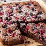 Wilgotne i puszyste ciasto czekoladowe bez glutenu z malinami i borówkami, pieczone z owocami na wierzchu, podane w naturalnym świetle na papierze do pieczenia.