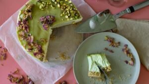 Bezglutenowy sernik pistacjowy z kremową masą i pistacjami na wierzchu podany na różowym tle