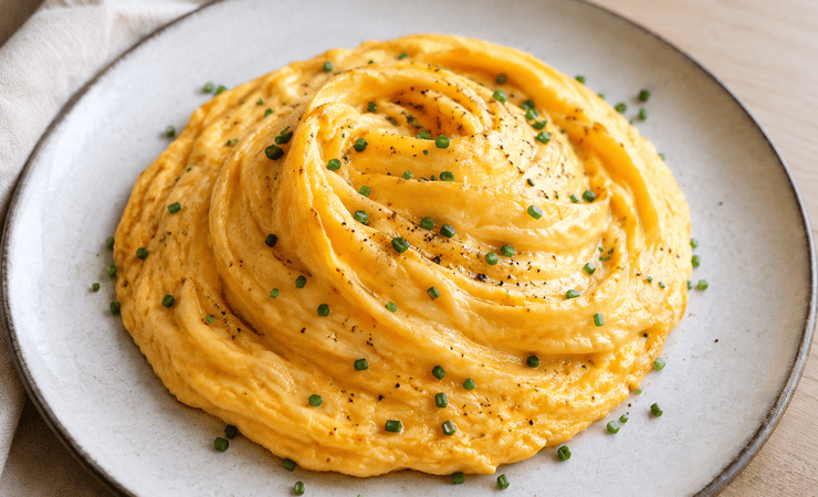 Puszysty omlet huragan o wirującej strukturze i kremowym środku podany na talerzu z posypką ze szczypiorku.