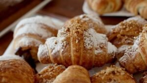 Kruche rogaliki bezglutenowe z nadzieniem, przygotowane z ciasta francuskiego bez glutenu i oprószone cukrem pudrem