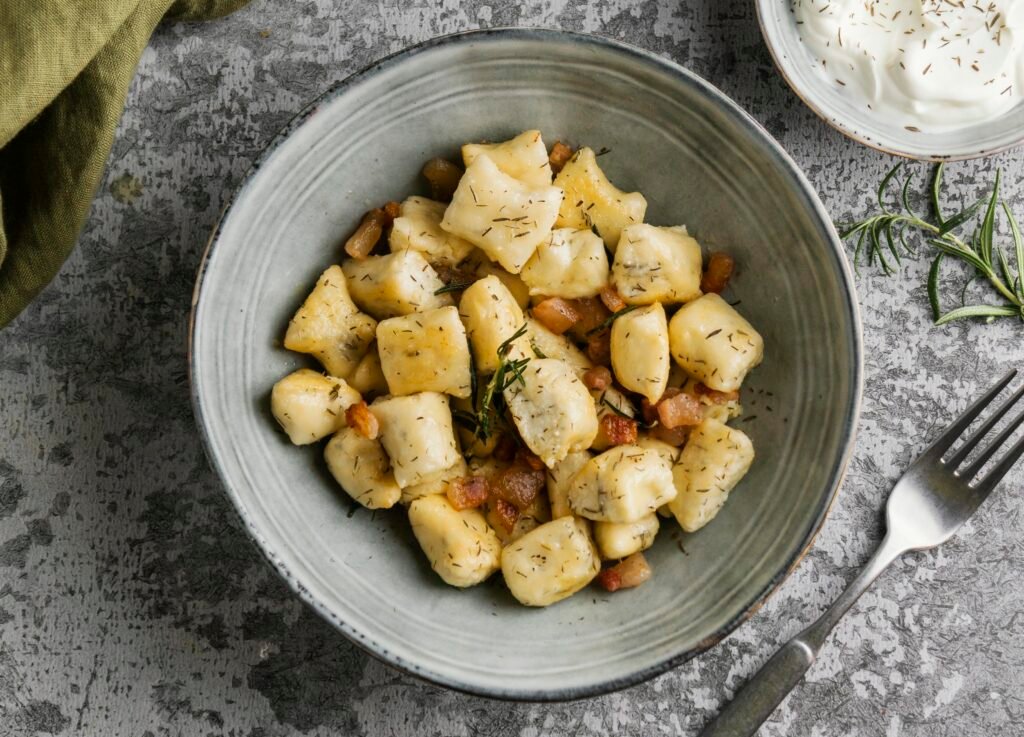 gnocchi bezglutenowe zdjęcie bezglutenowych gnocchi z dodatkami, podanych na głębokim talerzu z widelcem obok