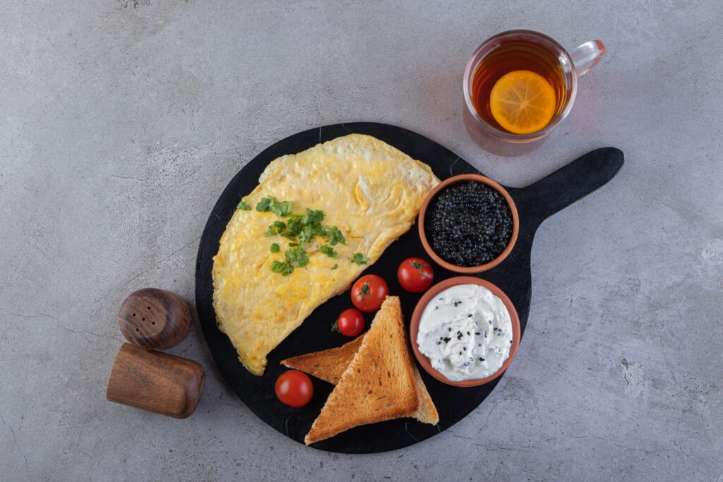 omlet z serka wiejskiego zdjęcie omletu z serka wiejskiego podanego na czarnej podstawce w towarzystwie szczypiorku, tostów, pomidorków, białego serka, kawioru i herbaty z cytryną