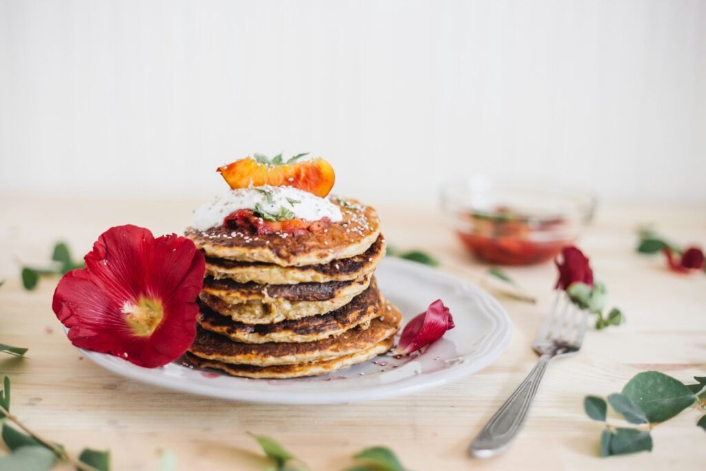 Bezglutenowe pancakes zdjęcie bezglutenowych pancakes ułożonych w stosik na talerzu udekorowanym kwiatami i liśćmi