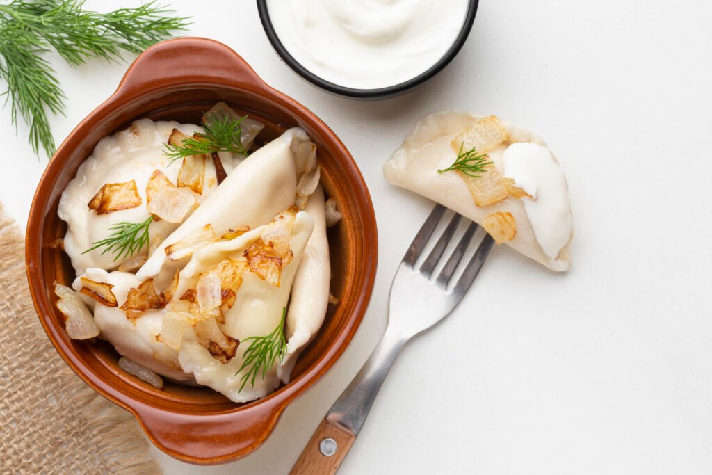 pierogi bezglutenowe zdjęcie pierogów bezglutenowych w glinianym naczyniu, ze smażoną cebulką z widelcem obok