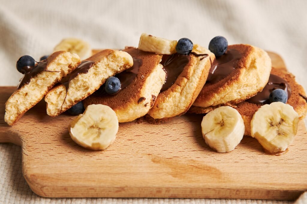 Placki bananowe z płatkami owsianymi zdjęcie bezglutenowych placków bananowych z z płatkami owsianymi podanych na drewnianej podstawce z kawałkami bananów, borówkami oraz bezglutenowym sosem czekoladowym