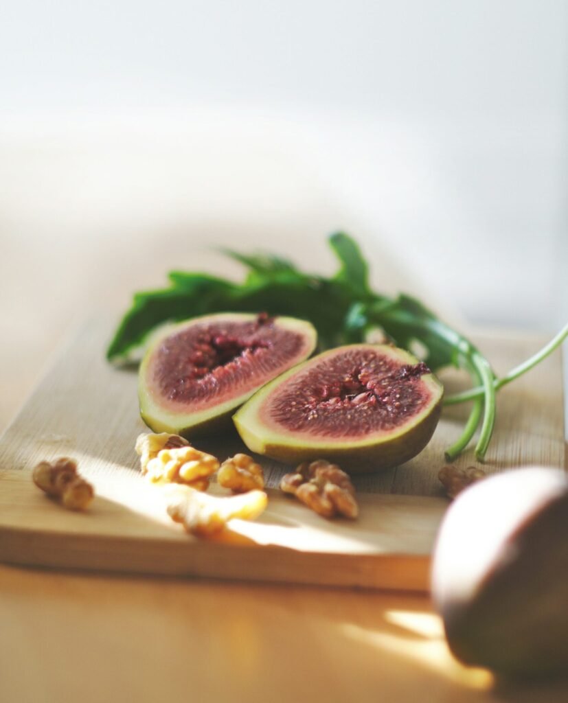 Zbliżenie na deskę do krojenia z połówkami świeżych fig, orzechami włoskimi i kilkoma liśćmi rukoli, oświetlone naturalnym światłem z boku.
