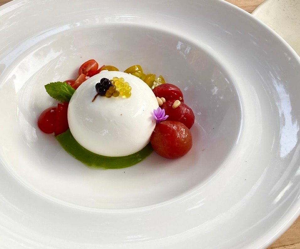 zdjęcie kulki bezglutenowej burraty ułożonej na zielonym pesto w owarzystwie pomidorków kokotajlowcyh na białym talerzu