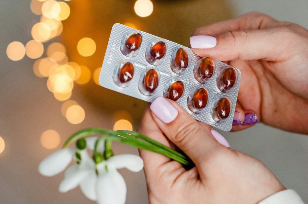 Jakie są konsekwencje nieprawidłowej diety bezglutenowej Dłonie trzymające blister z kapsułkami suplementów diety oraz biały kwiat przebiśniegu, symbolizujące zdrowie i profilaktykę