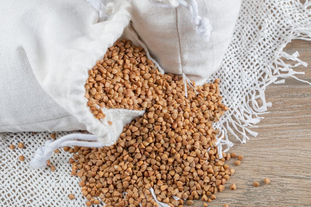 gryka bez glutenu zdjęcie gryki wysypującej się z białego woreczka na drewniany stół przykryty białym obrusem