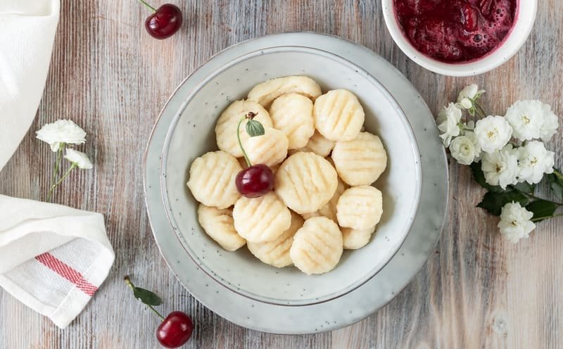 Bezglutenowe kluski leniwe na słodko z twarogu, podane w misce z wiśniami i sosem owocowym – delikatne pierogi leniwe bez glutenu.