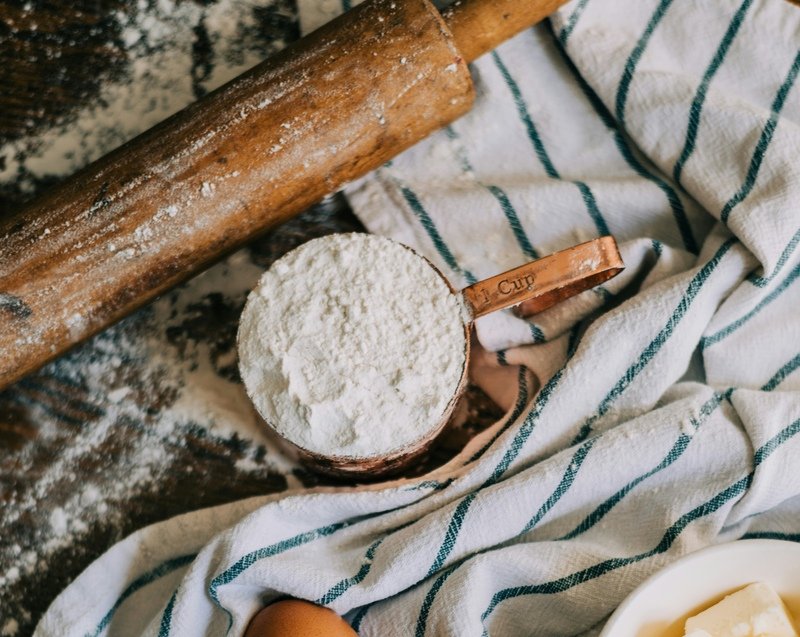 zdjęcie przestawiające stół z wałkiem, mąką i ścierką, zasypany mąką bezglutenową