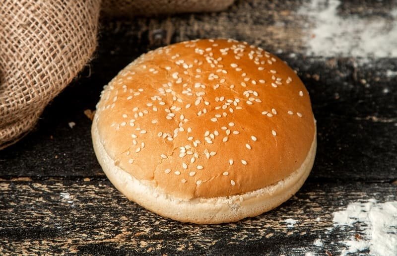 bezglutenowa bułka do burgerów posypana sezamem, upieczona na złoto, podana na ciemnym, rustykalnym blacie.