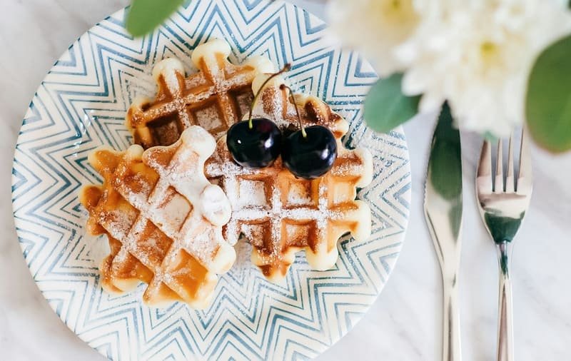 zdjęcie bezglutenowych gofrów na kolorowym talerzu, podane z wiśniami i cukrem pudrem