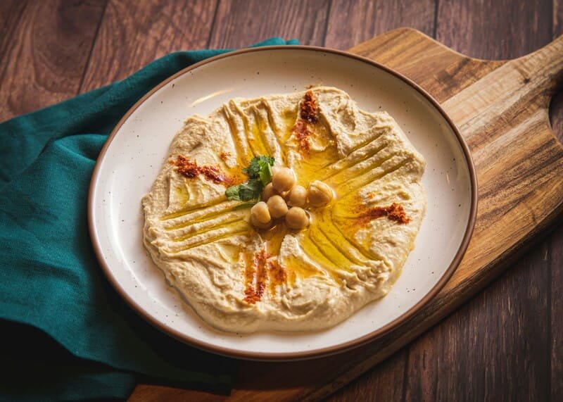 hummus naturalnie bezglutenowy hummus podany na białym talerzu z dodatkiem ziaren ciecierzycy i przypraw