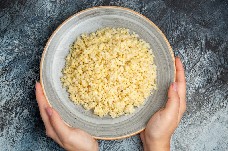 Kasza bulgur w misce trzymanej w dłoniach – pszenna kasza zawierająca gluten, niewskazana na diecie bezglutenowej i przy celiakii