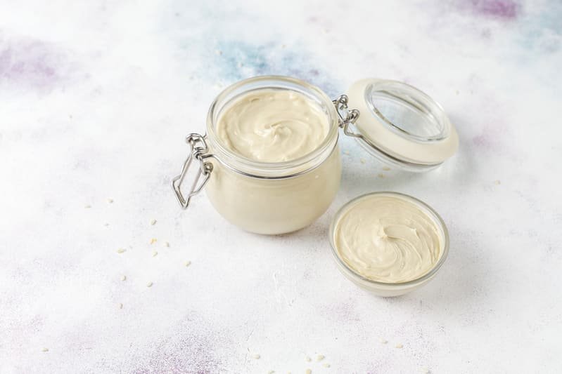 zdjęcie domowego majonezu bez glutenu w przezroczystym słoiczku z zamykaniem oraz w miseczce, na kolorowym tle