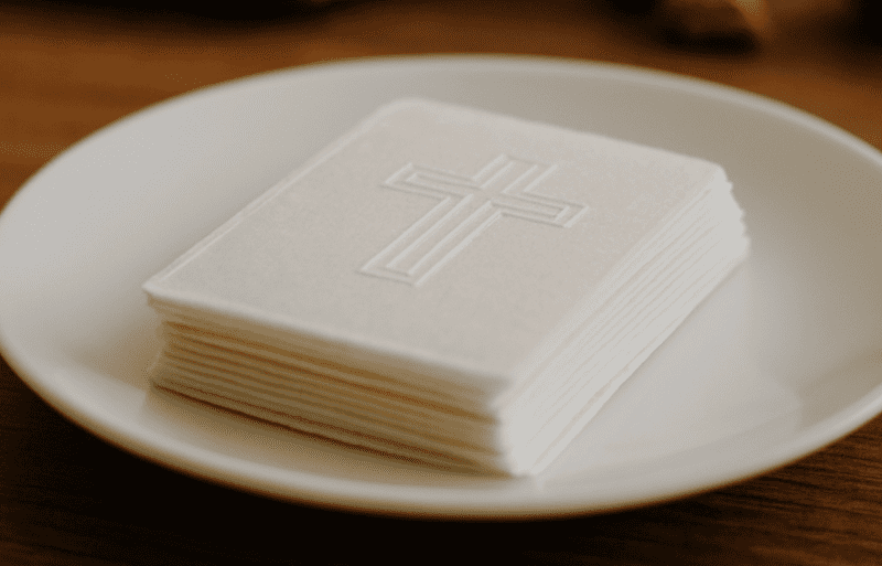 Opłatek wigilijny ułożony na białym talerzu w domowym otoczeniu, sfotografowany na drewnianym stole przy naturalnym świetle.