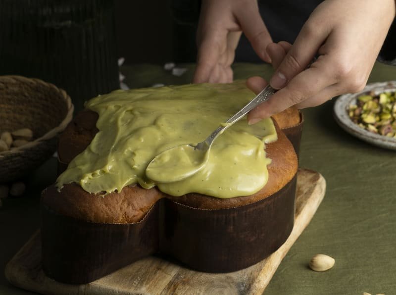 zdjęcie bezglutenowej pasty pistacjowej którą ręka rozsmarowuje na gotowym wypieku drożdżowym na kuchennym stole