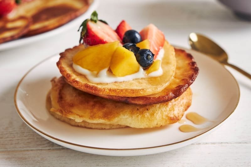 zdjęcie racuchów bezglutenowych ułożonych w stosik na talerzu i udekorowanych owocami